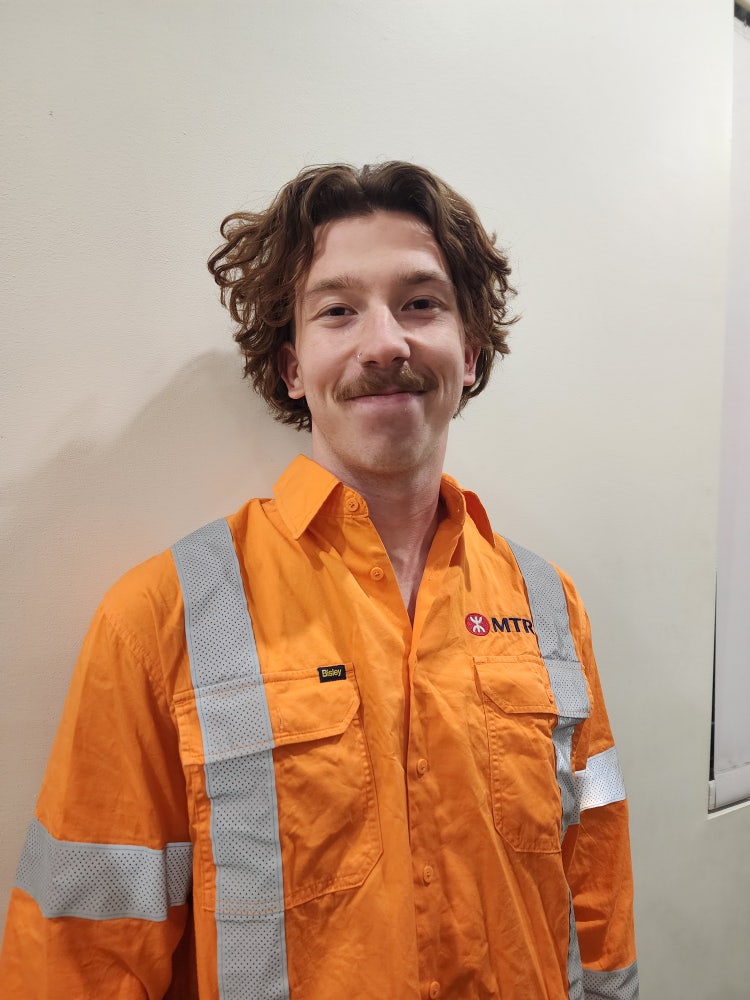 photo of person looking at camera, short brown wavy hair, wearing orange high visibility shirt
