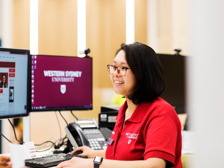 photo of person with fair skin and dark hair , wearing spectacles and a red shirt with a Western logo visible, sitting in front of a computer