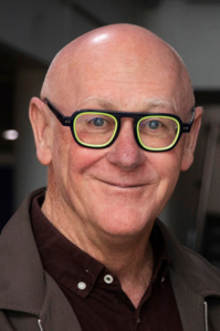 Leo wears a brown suit. He has black glasse with a neon green rim.